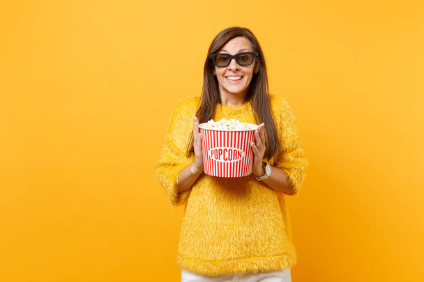 Ritratto di allegra bella ragazza in maglione di pelliccia, occhiali 3d imax guardare film con secchio di popcorn isolato su sfondo giallo brillante. Persone emozioni sincere nel cinema, stile di vita
 - Foto, immagini
