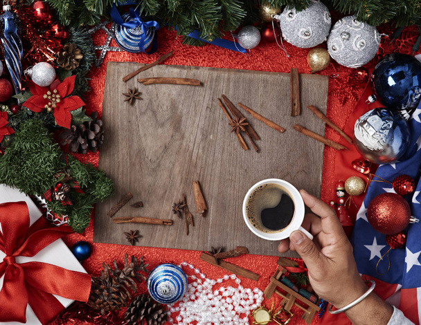 Manos masculinas con copa de bebida de invierno en la mesa de madera roja con regalo de Navidad y decoraciones, fondo de Año Nuevo, laico plano. Diseño con espacio libre de texto
. - Foto, imagen