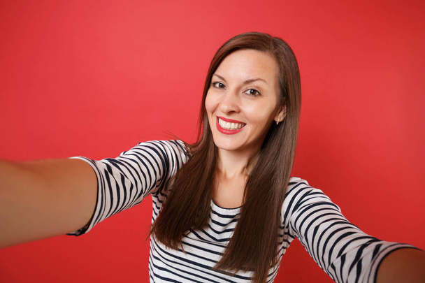 Nahaufnahme Selfie-Aufnahme der schönen lächelnden jungen Frau in lässiger gestreifter Kleidung isoliert auf leuchtend rotem Wandhintergrund. Menschen aufrichtige Emotionen Lifestyle-Konzept. Attrappe Kopierfläche für Werbung - Foto, Bild