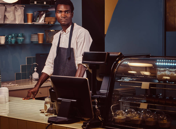 Portrait of a handsome African barista at counter of a trendy coffee shop. - Foto, imagen
