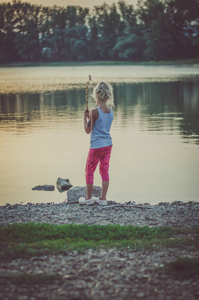 adorable little girl fishing with home made fishing rod at the pond at the sunset - Photo, Image