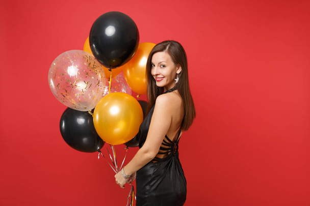 Smiling young girl in little black dress celebrating holding air balloons isolated on red background. St. Valentine's, International Women's Day, Happy New Year, birthday mockup holiday party concept - Photo, Image