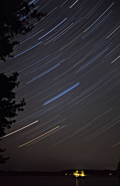 Senderos de estrellas de larga exposición girando alrededor de la Estrella del Norte. Cabaña luces abajo en el horizonte
. - Foto, imagen