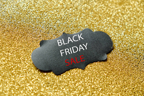 Black friday sale concept. Fourth Friday of November, beginning of Christmas shopping season since 1952. Black tag w/ white text on golden glitter background. Copy space, close up, top view, flat lay. - Fotó, kép