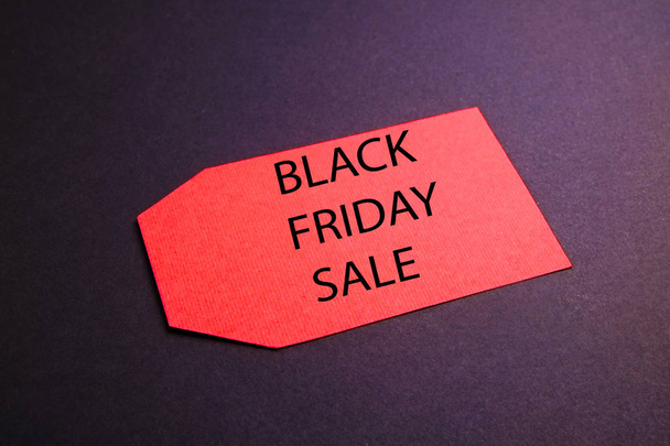 Black friday sale concept. Fourth Friday of November, beginning of Christmas shopping season since 1952. Red tag with black text on bright red background. Copy space, close up, top view, flat lay. - Photo, Image