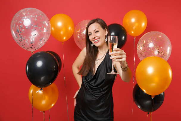 Hermosa chica en vestido negro celebrando, señalando la mano con una copa de champán en la cámara sobre globos de aire de fondo rojo brillante. Día de la Mujer, Feliz Año Nuevo, concepto de fiesta de cumpleaños simulada
 - Foto, Imagen