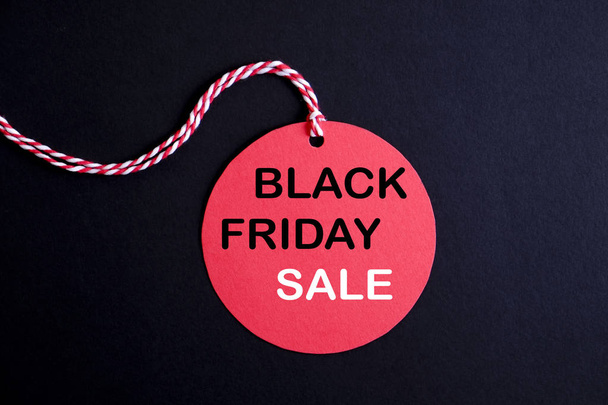 Black friday sale concept. Fourth Friday of November, beginning of Christmas shopping season since 1952. Red tag with black text on bright red background. Copy space, close up, top view, flat lay. - Фото, изображение