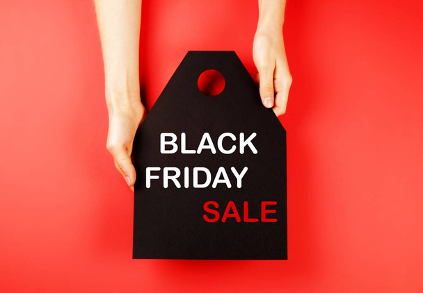 Black friday sale concept. Fourth Friday of November, beginning of Christmas shopping season since 1952. Black tag with white text on bright red background. Copy space, close up, top view, flat lay. - Foto, Imagem
