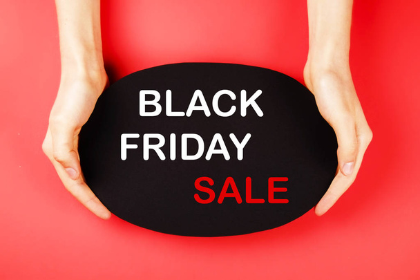 Black friday sale concept. Fourth Friday of November, beginning of Christmas shopping season since 1952. Black tag with white text on bright red background. Copy space, close up, top view, flat lay. - Фото, изображение