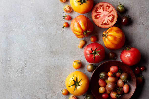Fresh various colorful tomatoes on gray marble background. Top view. Free empty space for text - Photo, Image