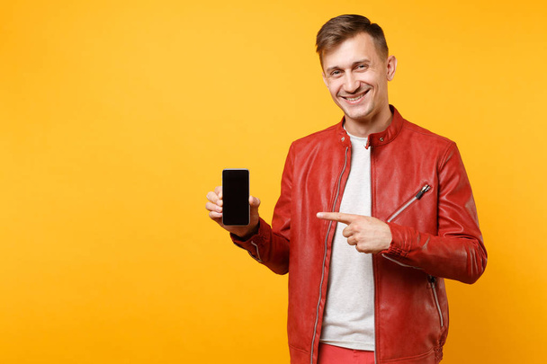 Портрет моды весело молодой человек в красной кожаной куртке, футболка держать мобильный телефон с пустым пустым экраном изолированы на ярко-желтом фоне. Люди искренние эмоции концепции образа жизни. Рекламная зона
 - Фото, изображение