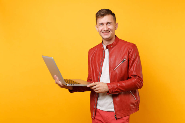 Portrait vogue amusant beau jeune homme en veste en cuir rouge, t-shirt en utilisant ordinateur portable pc comprimé isolé sur fond jaune tendance lumineux. Les gens sincères émotions concept de style de vie. Espace publicitaire
 - Photo, image