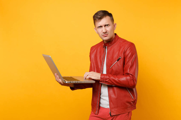 Portrait vogue amusant beau jeune homme en veste en cuir rouge, t-shirt en utilisant ordinateur portable pc comprimé isolé sur fond jaune tendance lumineux. Les gens sincères émotions concept de style de vie. Espace publicitaire
 - Photo, image