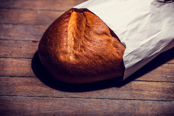 Вкусный хлеб в бумаге на деревянном столе. Вид сбоку
 - Фото, изображение