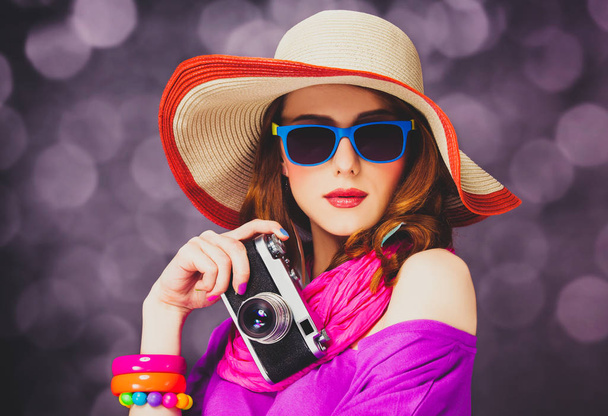 Funny redhead girl in hat with camera on bokeh background - Fotó, kép
