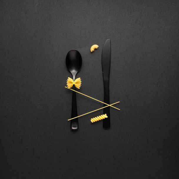 Creative still life photo of fork and spoon with raw pasta on black background. - Fotoğraf, Görsel