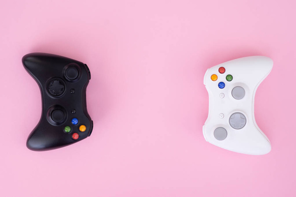 Twee joysticks, zwart-wit op een pastel roze achtergrond. Witte en zwarte gamepad zijn geïsoleerd op een pastel roze achtergrond. Gaming competitie. Gamer concept. Copyspace - Foto, afbeelding