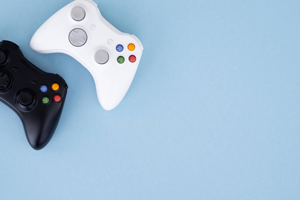 White and black gamepad are isolated on a pastel blue background. Two joysticks, black and white on a pastel blue background. Computer game competition. Gamer concept. Copyspace - Photo, Image
