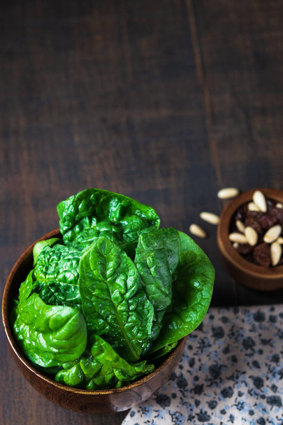 Fresh spinach with raisins, pinions in a wooden bowl on rustic wooden background, selective focus. Vertical. Spase for text. - Photo, Image