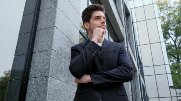 Portrait of successful pensive businessman in city. Man in business suit jacket on office building background. Handsome person ponders about work. Camera moves from right to left - Séquence, vidéo
