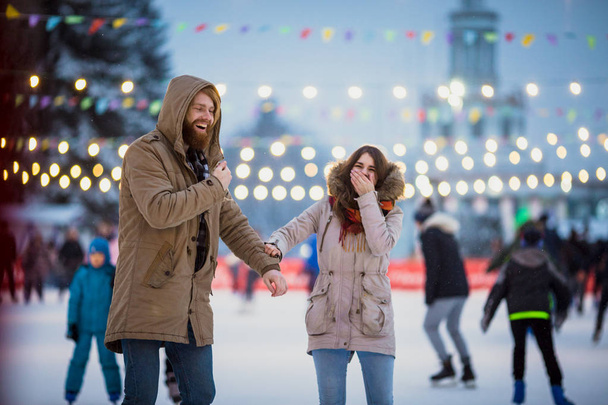 Молода пара в любите Кавказький чоловік з світлим волоссям з довгим волоссям, і бороди і красива жінка весело, активний дату на ковзанах на льоду арени в площі міста вечір взимку напередодні Різдва - Фото, зображення
