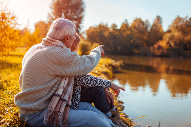 秋の湖でピクニックを持つ年配のカップル。幸せな男と女の自然との触れあいと抱き締めます。男の距離を指す - 写真・画像