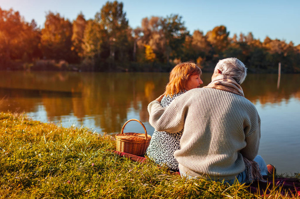 Seniorenpaar beim Picknick am Herbstsee. glückliche Männer und Frauen genießen die Natur und umarmen sich. friedliche Landschaft - Foto, Bild