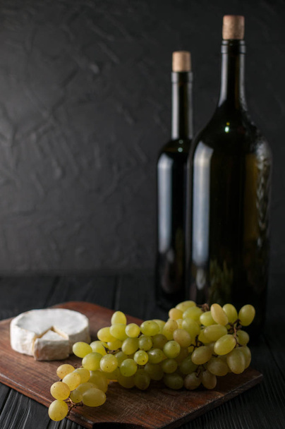 Bouteilles de vin sur fond de bois noir avec raisins et fromage Camemberg
 - Photo, image