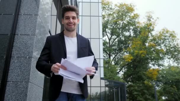 Businessman throwing papers documents into air and celebrates success on office building background. Freedom, successful completion of project concept. Steadicam 4k footage - Video