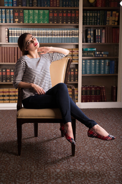 Young caucasian woman dressed in mid century casual fashion poses in a library - Foto, Imagen
