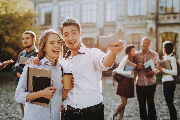 Selfi. Holding Books. Standing in University. Good Mood. Intelligence. Man and Woman. Standing Together. Outside. Sunny Day. Students. Friends. Happy. Courtyard. Books. University. Knowledge. - 写真・画像