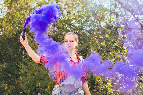 Young mixed race woman dressed in grungy hipster style outdoors poses with colored smoke bombs - Photo, Image