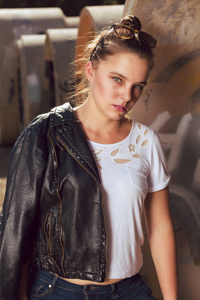Young mixed race woman dressed in retro biker style outdoors poses in an industrial area - Φωτογραφία, εικόνα