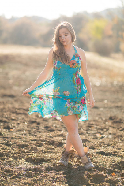 Happy young mixed race woman in blue dress poses in field destroyed by wildfire while covered in ashes - Photo, Image