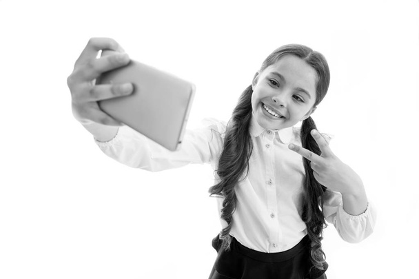 Happy girl take selfie isolated on white. Child smile with victory hand gesture on smartphone. digital marketing in virtual world. Selfie fun. Cute blogger make video call. Modern life and technology - 写真・画像