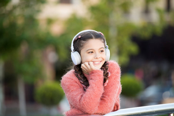 Funny cool stylish girl is listening to music and thinking about positiveness. Girl standing on the bridge with headphones. Tranquil influence of music. Nice girl in pink sweater enjoying song - Φωτογραφία, εικόνα
