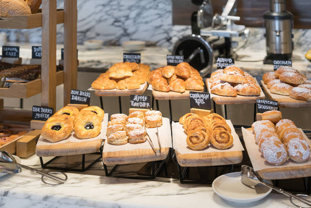Frühstück in verschiedenen Geschmacksrichtungen Danishs, Brötchen und Muffins in hölzernen Tabletts im Hotelrestaurant - Foto, Bild