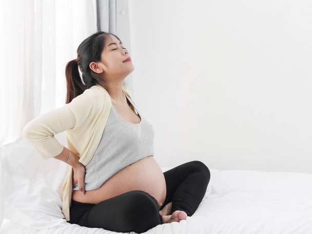 Pregnant Asian woman with back pain in front of a window, healthy concept. - Foto, Imagem
