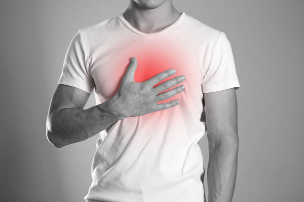 The man is holding his chest. Chest pain. Heartburn. The hearth is highlighted in red. Close up. Isolated background. - Foto, imagen
