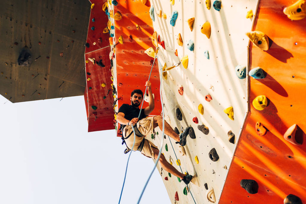 Een man die een touw draagt, klimmend op een zeer hoge rotsklimwand. - Foto, afbeelding