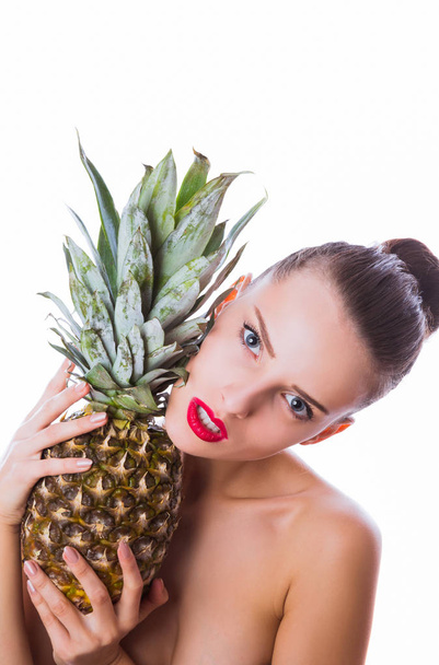 Portrait of pretty, serious woman who keeps a pineapple near her face against white background indoor - Foto, imagen