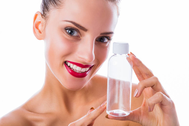 Close-up wonderful, smiling woman keeps empty bottle in hand near her face on the white background - Фото, изображение