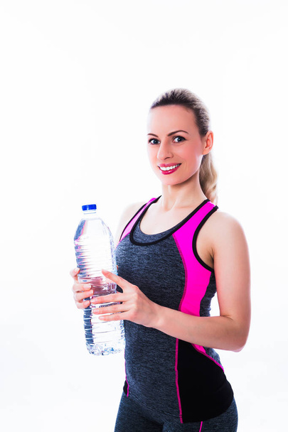 Portrait of sporty smiling woman in sport dress who keeps a bottle of water on the white background - Foto, Bild