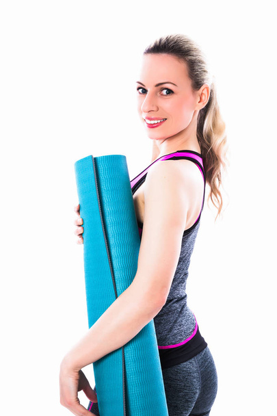 Cheerful sporty woman stands in sport dress and keeps carpet against the white background - Фото, зображення