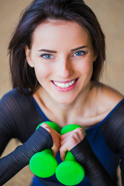 Close-up face of sporty woman who smiles and keeps the dumbbells in hands outdoor - Fotografie, Obrázek
