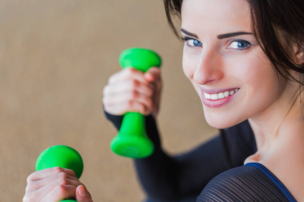 Close-up smiling sporty woman keeps the green dumbbells in hands outdoor - Фото, зображення