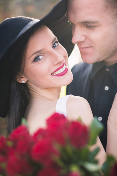 Smiling stylish couple with roses, he looks at her, outside - Foto, Imagen