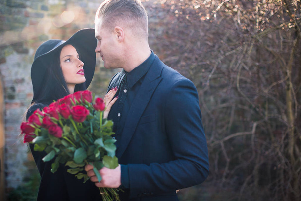 Attractive couple in black, looks at each other, with flowers, outdoor - Foto, Bild