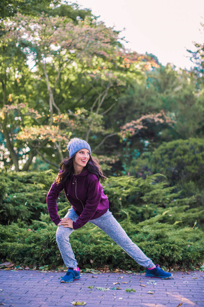 Young sporty woman stands in the park and does exercise and looks aside - Photo, image