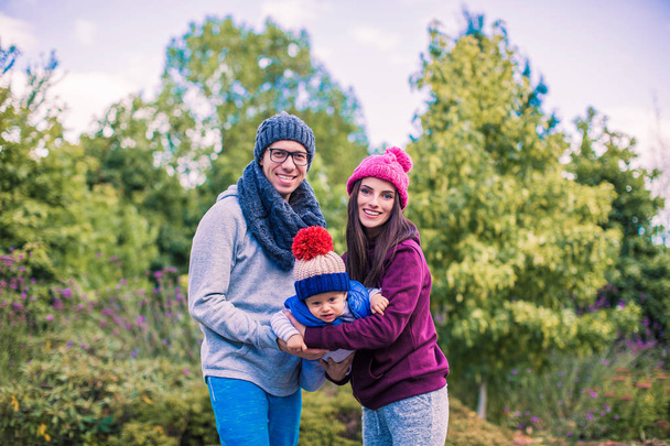 Nuori onnellinen perhe seisoo puistossa ja vanhemmat pitävät pienen poikansa
 - Valokuva, kuva